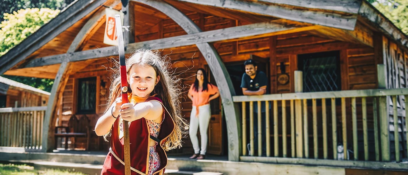 Girl doing archery outside a woodland lodge at Warwick Castle